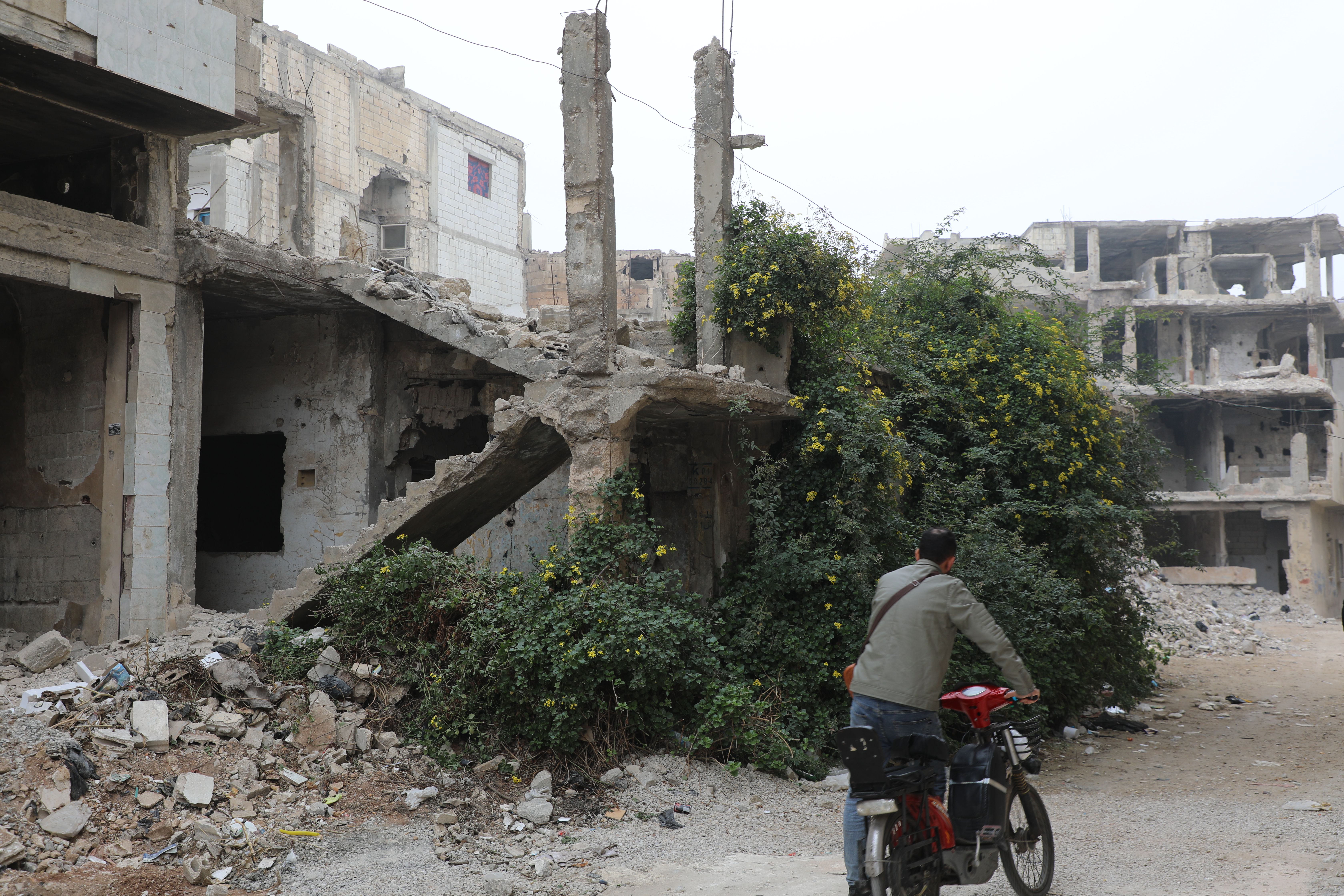 man biking in a street with destroyed houses