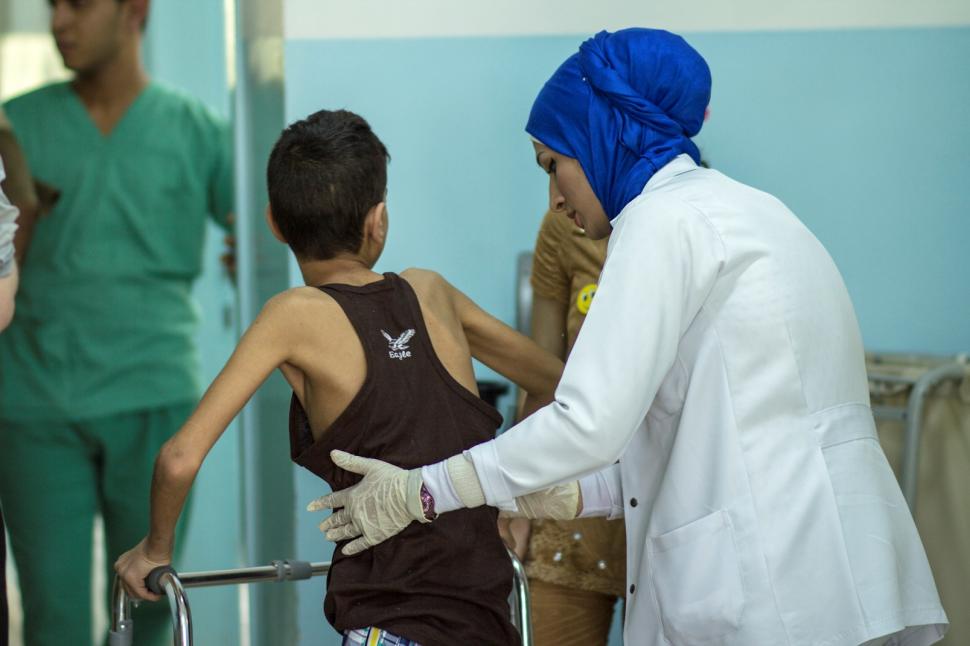 Fysiotherapeute Rula helpt het jongetje Fawzi overeind na zijn fysiotherapiesessie. Jordanië, Ramtha ziekenhuis, juni 2015.