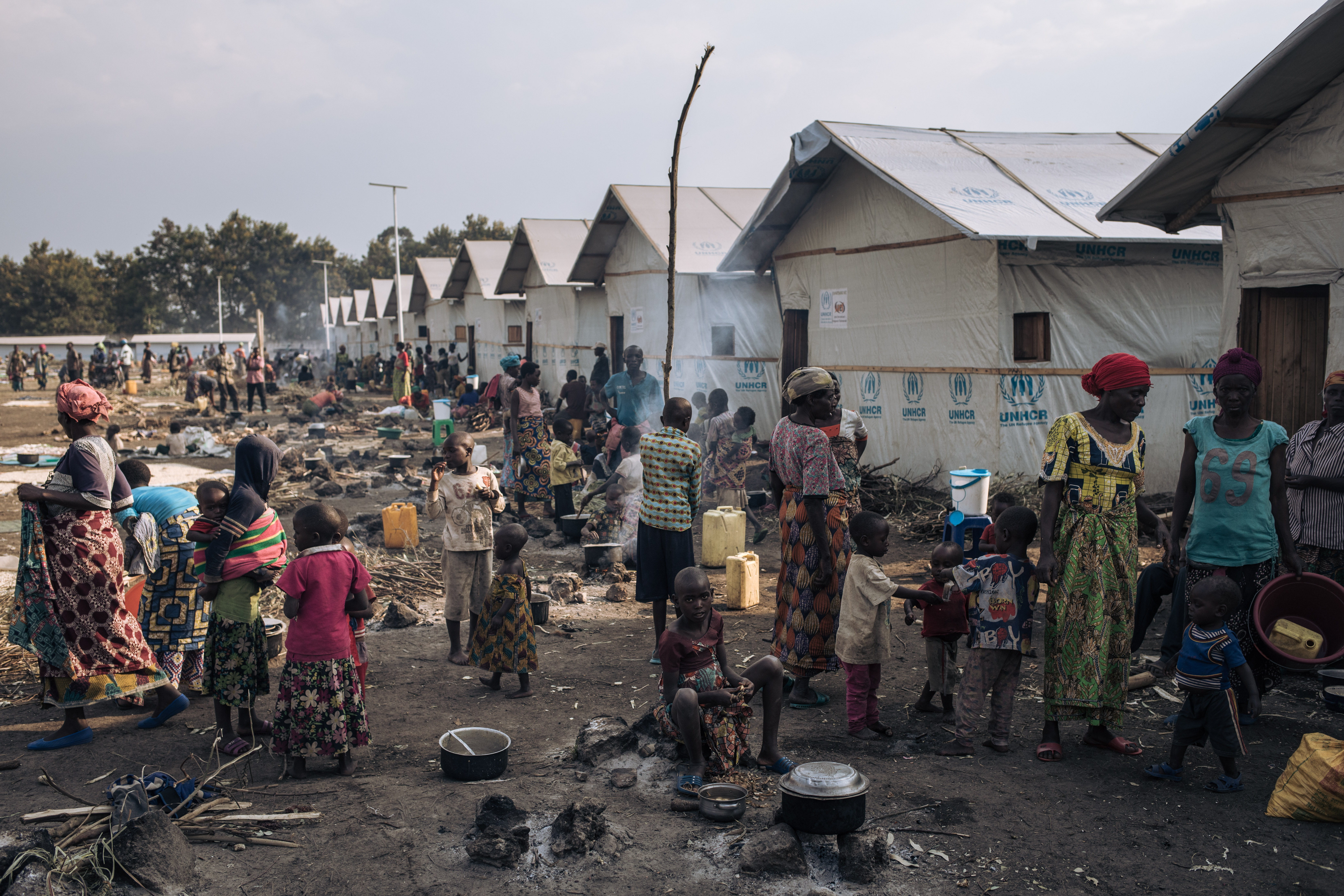 Des personnes déplacées, dont des enfants, préparent de la nourriture devant des abris communautaires sur le site informel de déplacés du stade de Rugabo, dans le centre de Rutshuru, dans la province du Nord-Kivu, à l'est de la République démocratique du Congo.