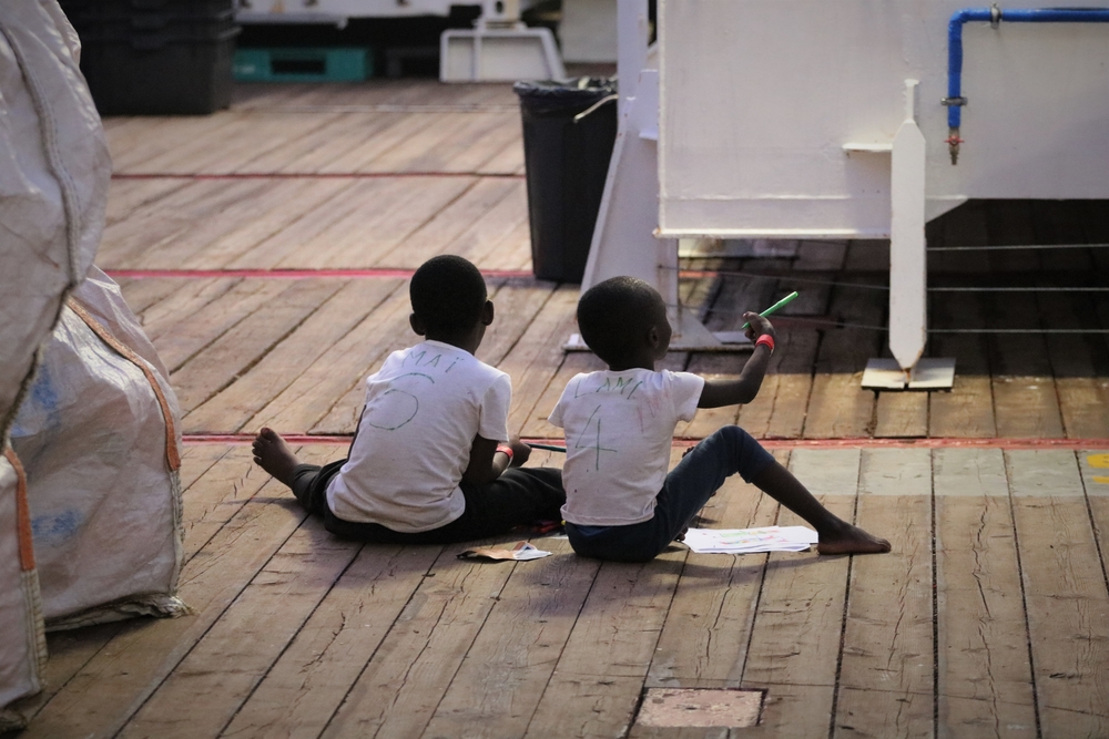 Twee geredde kinderen aan boord van het schip maken samen een tekening. © 