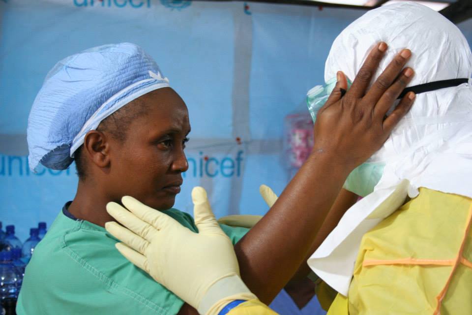 Een medewerker van Artsen Zonder Grenzen trekt het beschermende pak aan om ebolapatiënten te kunnen verzorgen. Een collega controleert nauwlettend of alle veiligheidsvoorschriften gevolgd worden. ELWA 3, Monrovia. © Caroline Van Nespen/AZG. 
