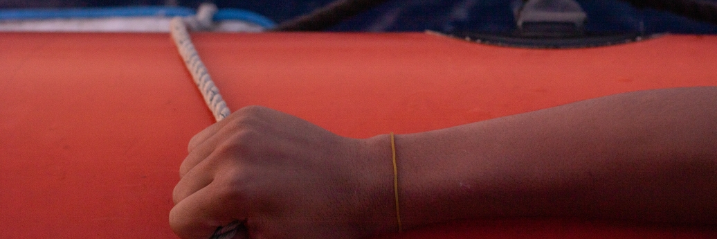 Une main tient la corde sur un canot de sauvetage rouge.