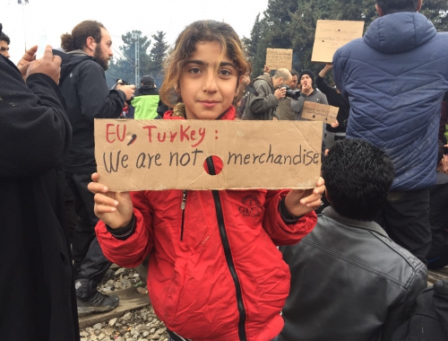Une enfant syrienne dans un camp de réfugiés à la frontière entre la Grèce et la Macédoine montre une pancarte avec un message à l'attention des dirigeants européens et turcs: 'Nous ne sommes pas une marchandise'. © Gemma Gillie/MSF. Idomeni, 2016.