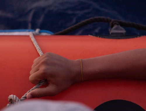 Een hand houdt het touw op een rode reddingsboot vast. 