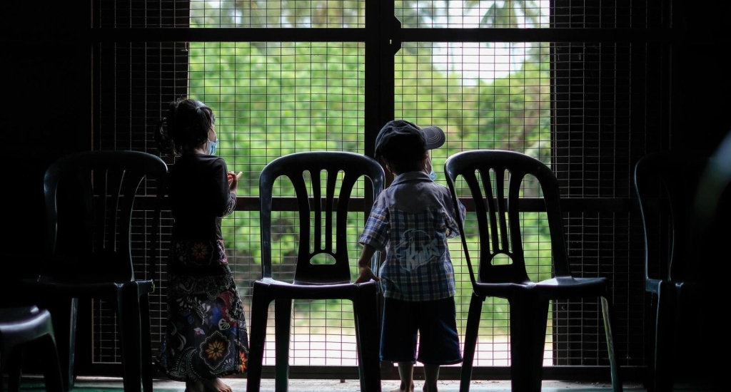 Een tweeling kijkt uit het raam van de wachtkamer van de mobiele kliniek van AzG in Penang