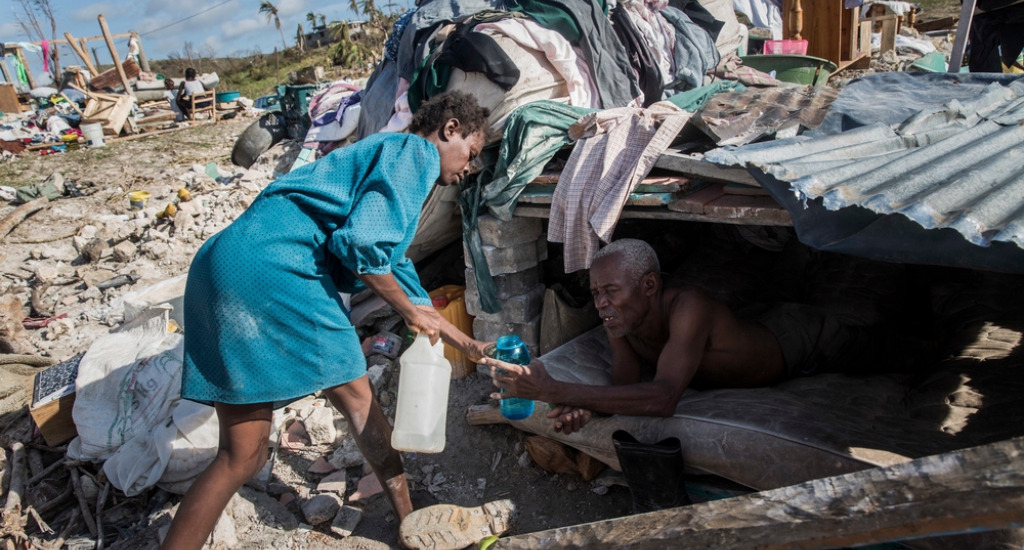 Un homme est trop malade pour marcher, sa femme lui apporte de l'eau sous un abri de fortune car leur maison a été détruite après le passage de l'ouragan © Andrew McConnell. MSF. Haïti, 2016.