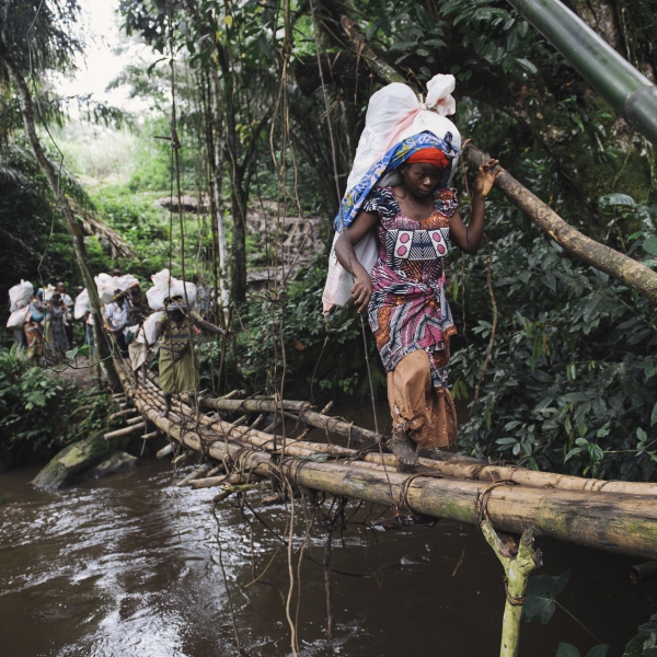 Des membres du PUC portent des sacs qui seront nécessaires à la mise en place d’une vaccination. Ils traversent un pont réalisé en bambou.  © Phil Moore 
